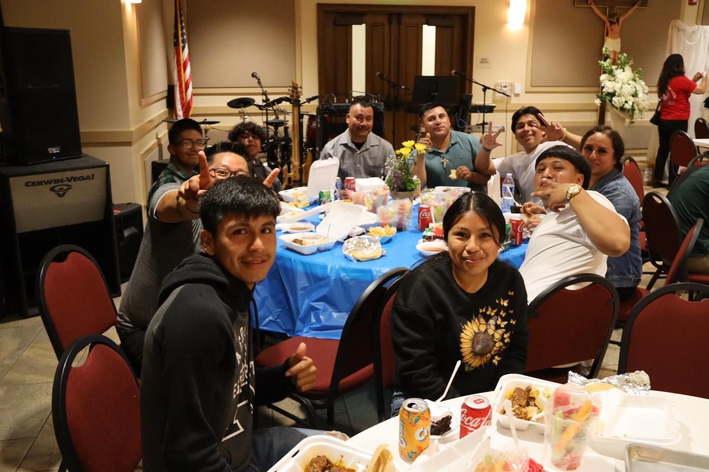 People gathered around blue banquet tables at an indoor social event, smiling at the camera.