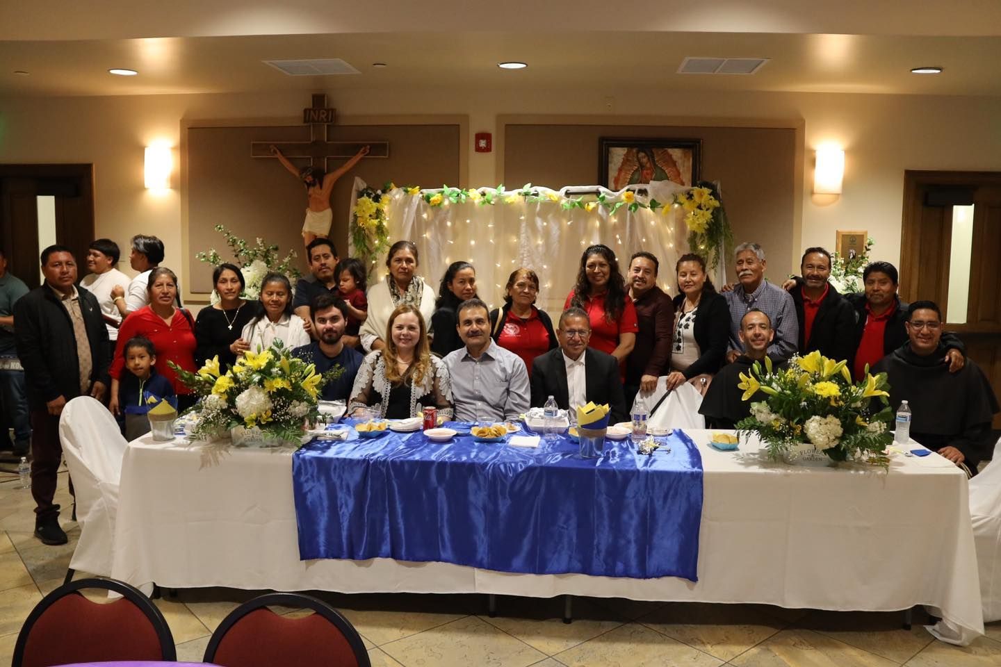 Large group gathered behind a decorated banquet table in a warmly lit hall, posing for a photo