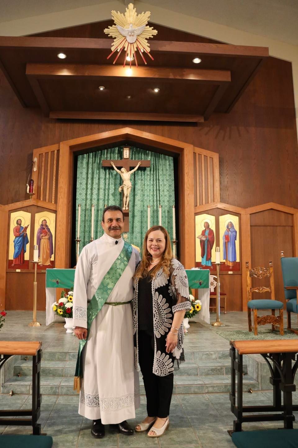 Two people stand before a church altar with a crucifix and green drapery.