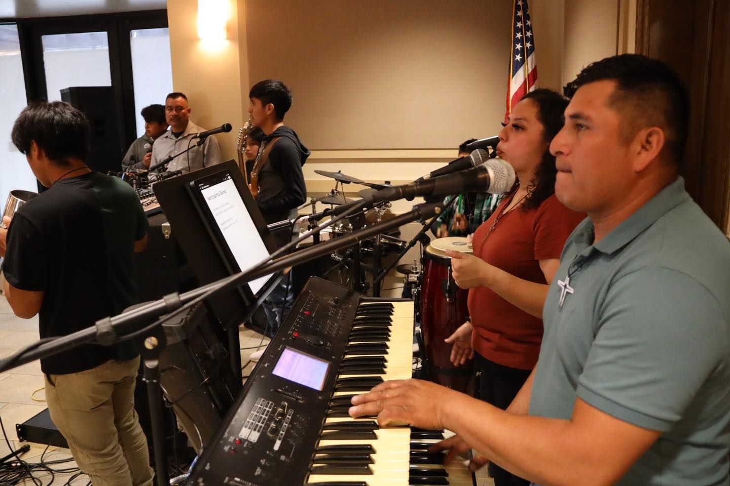 Musicians performing indoors, with keyboard and brass instruments in a conference room