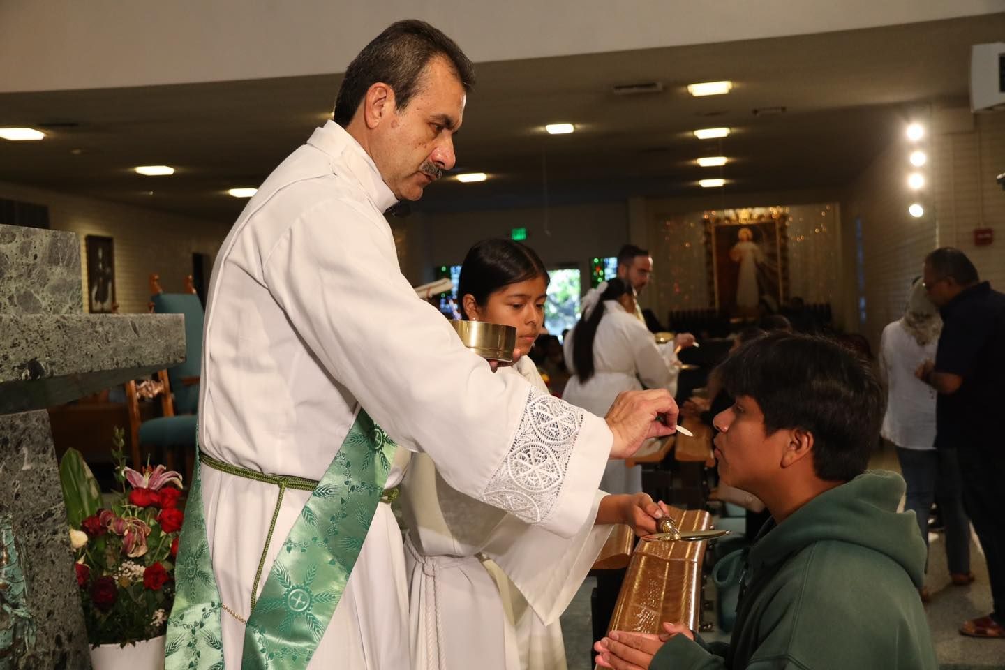 Priest in white vestments giving communion to a seated man in a church interior