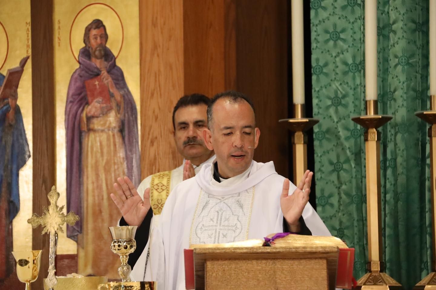 Priest speaking at a church altar with candles and a religious icon in the background