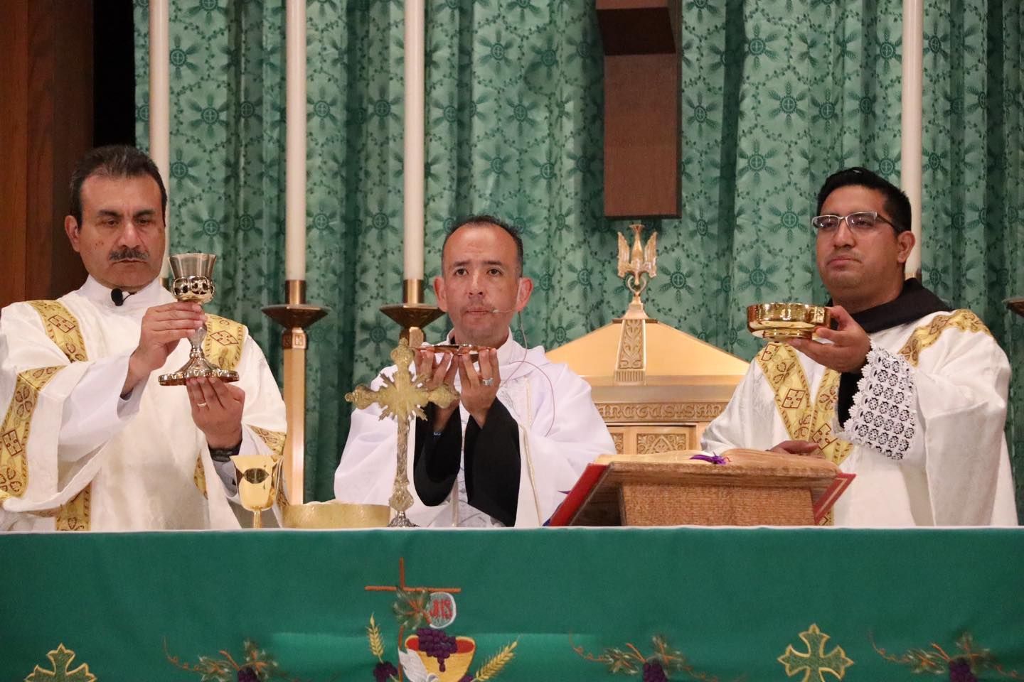 Three priests hold up chalices during a church service at the altar.