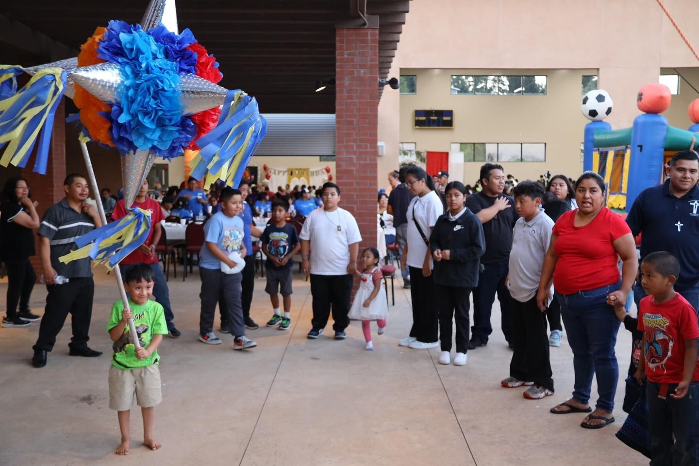 Crowd gathered outdoors beside a colorful piñata and streamers at a festive event