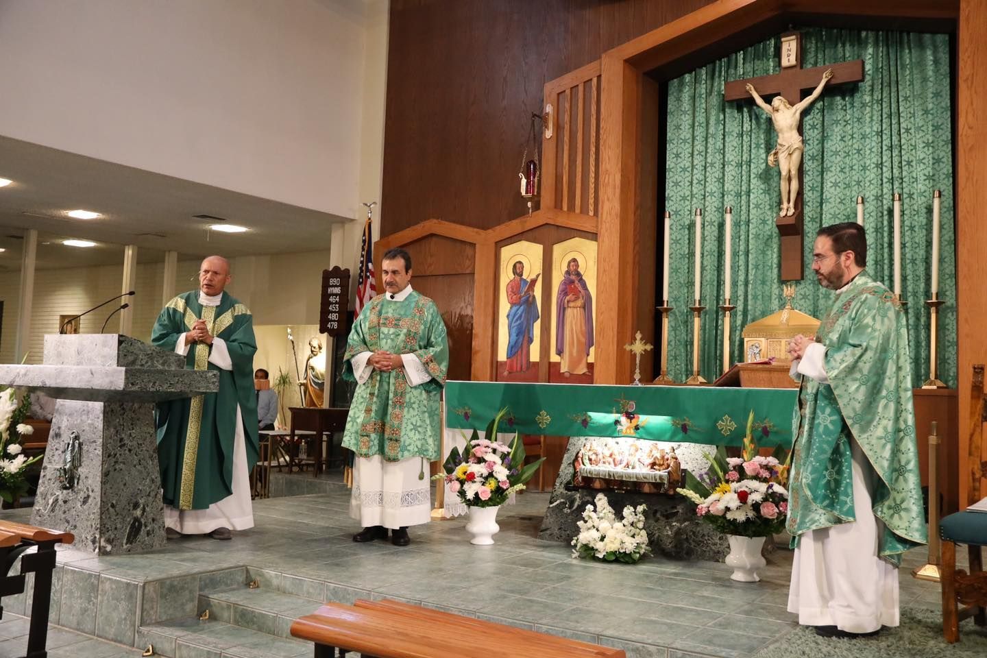 Three priests in green vestments stand at an altar during a church service.