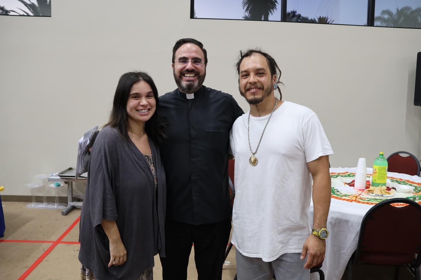 Three people smiling indoors at a table with drinks and snacks