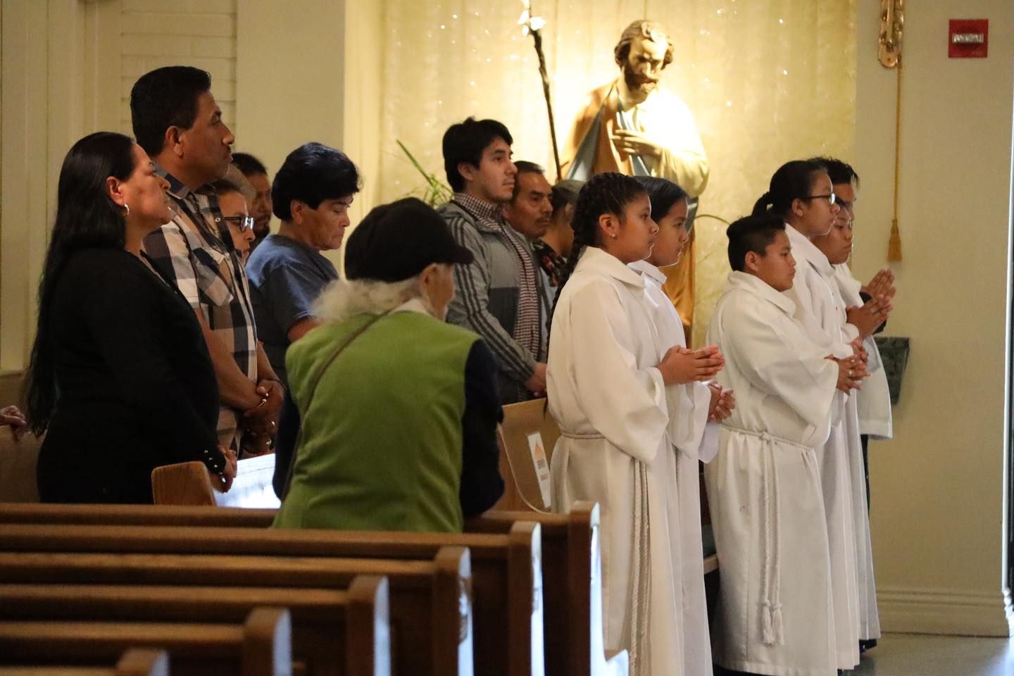Church service with several people standing in prayer near the altar, including white-robed clergy.