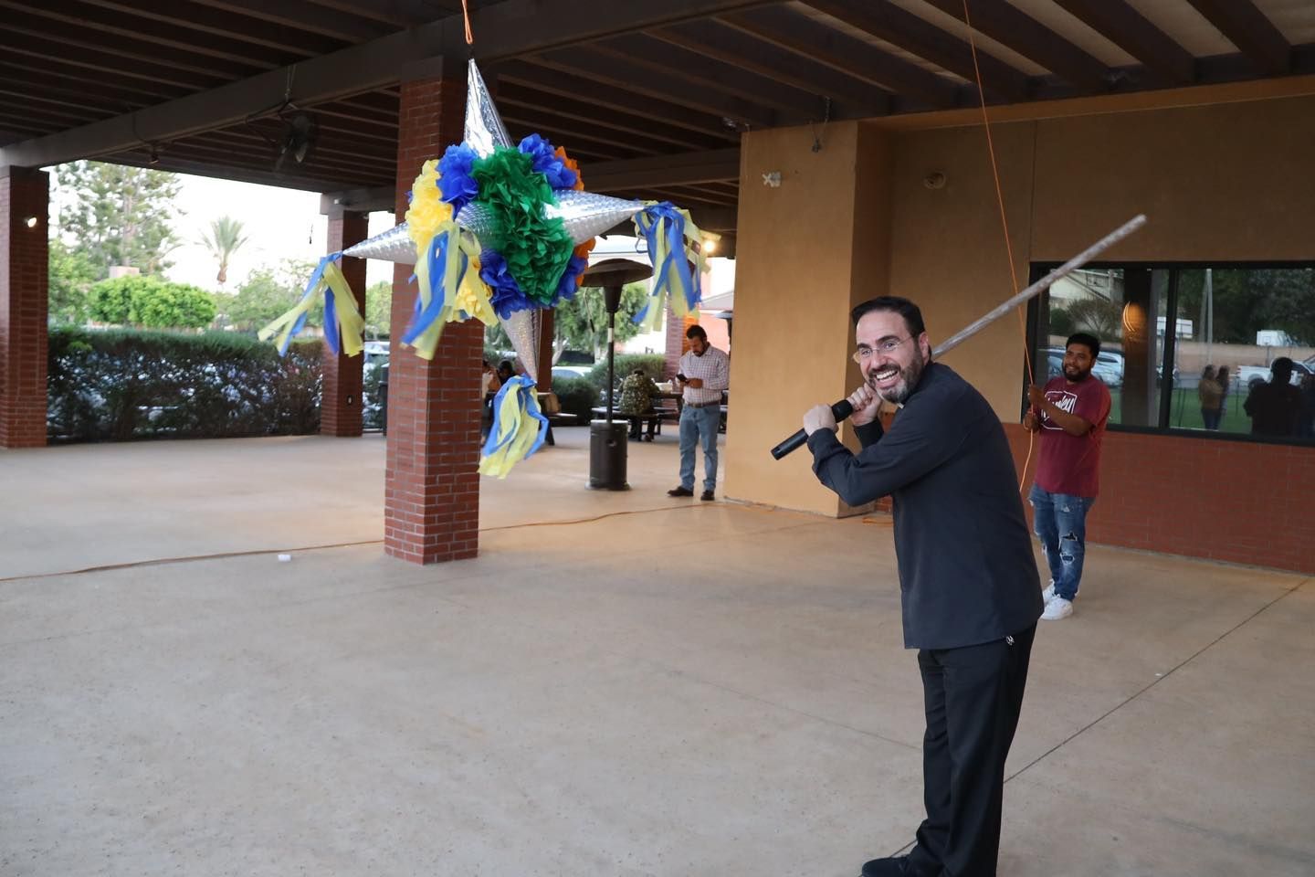 Man playing a trumpet outdoors under a covered walkway, with colorful decorations in the background.