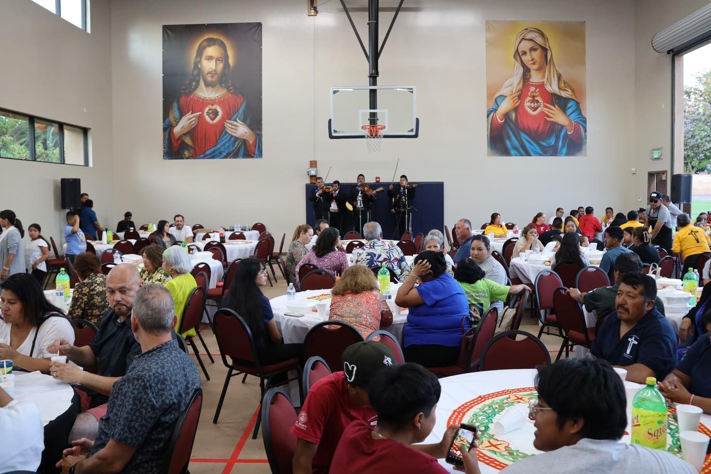 Crowded indoor banquet with people seated at tables, a stage, and large religious portraits on the wall