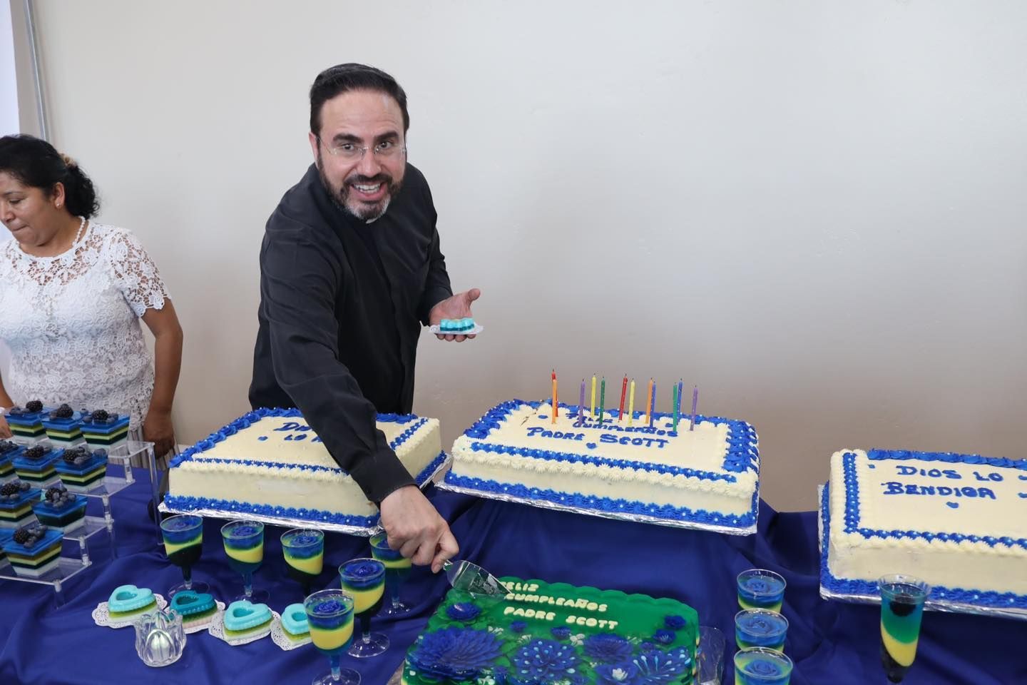Man serving drinks at a dessert table with blue and white cakes and cupcakes at a celebration
