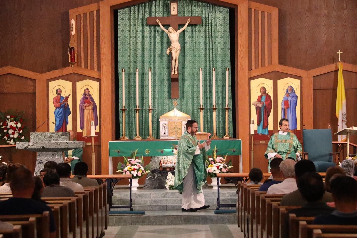 Priest celebrating Mass at a church altar with crucifix and congregants seated in pews