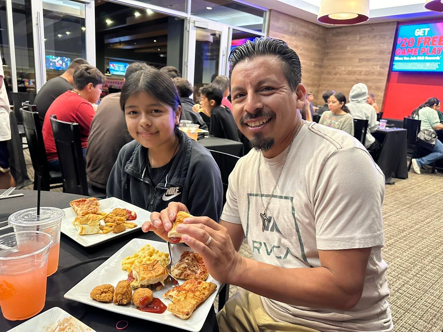 Two people smiling at a restaurant table with plates of food and drinks.