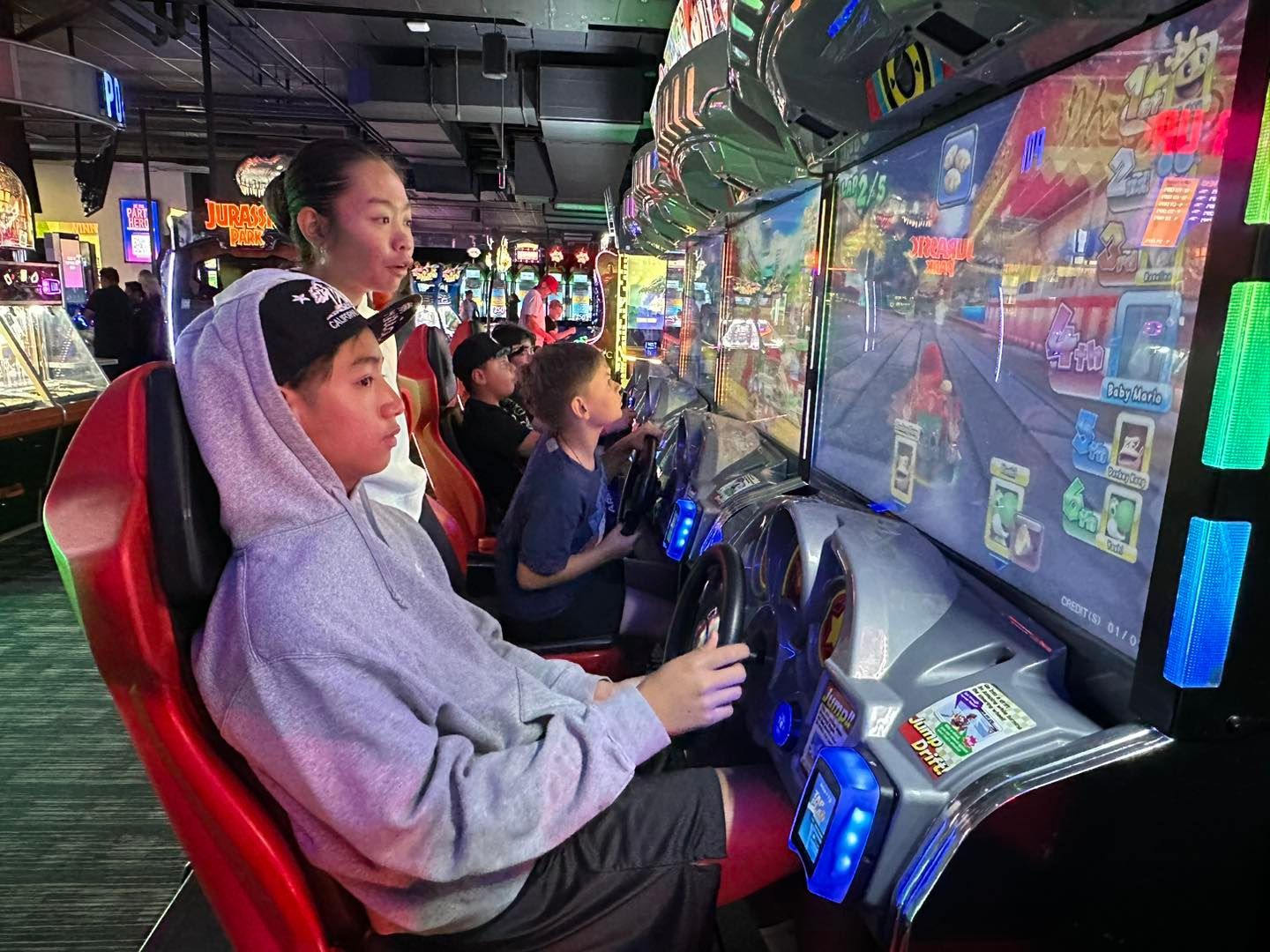 Kids playing racing arcade games in a neon-lit arcade, focused on the screens.