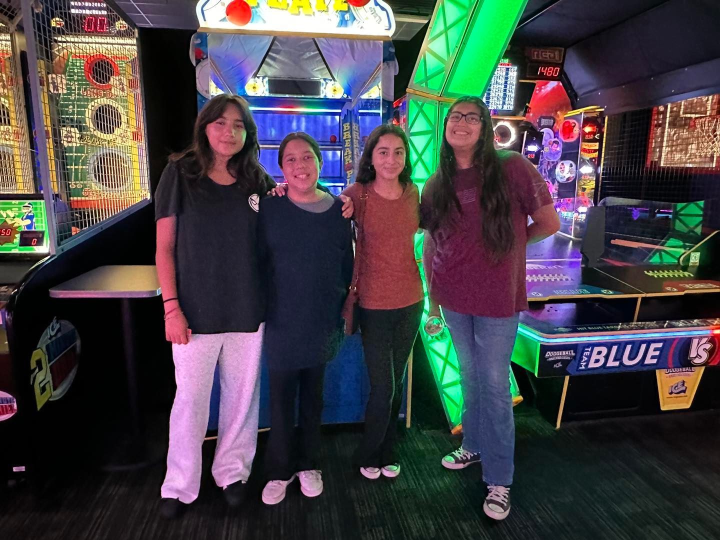 Four people standing in a neon-lit arcade beside arcade machines