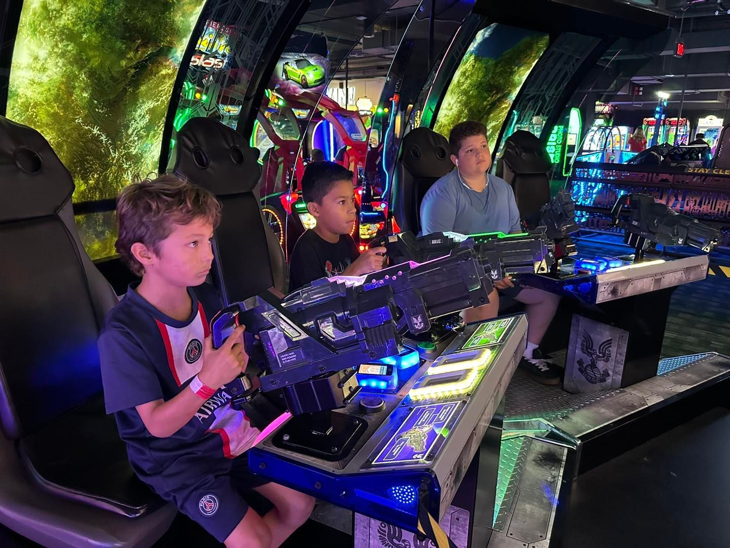 People playing arcade laser tag in a neon-lit venue, aiming large blasters at targets.