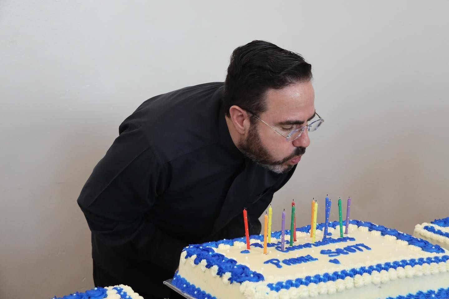 Man leaning over a frosted birthday cake with lit candles and blue icing decorations