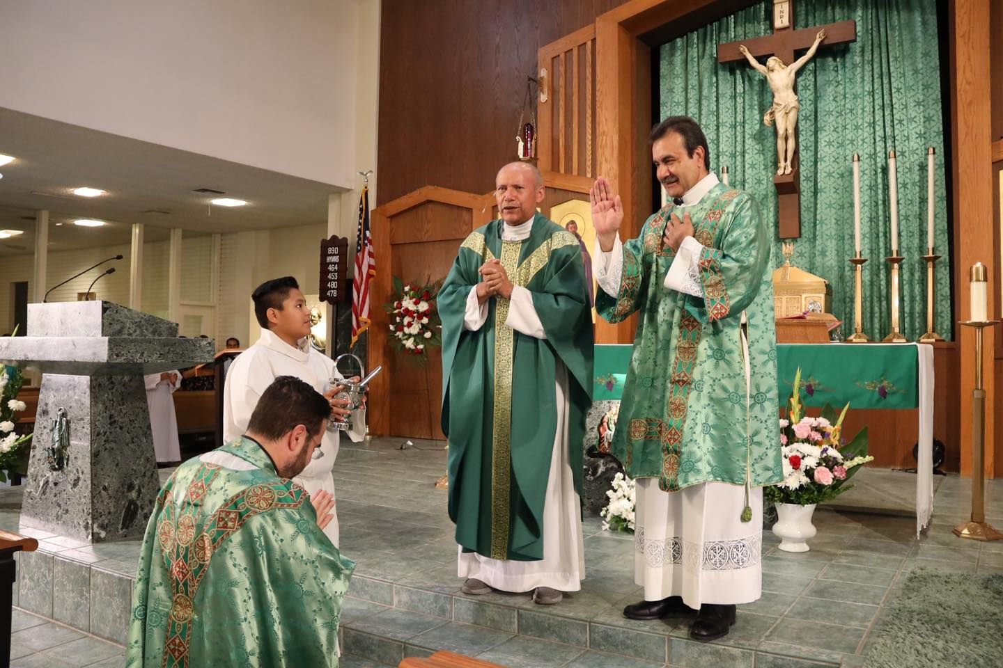 Priests in green vestments celebrate Mass at an altar with a crucifix in a church.