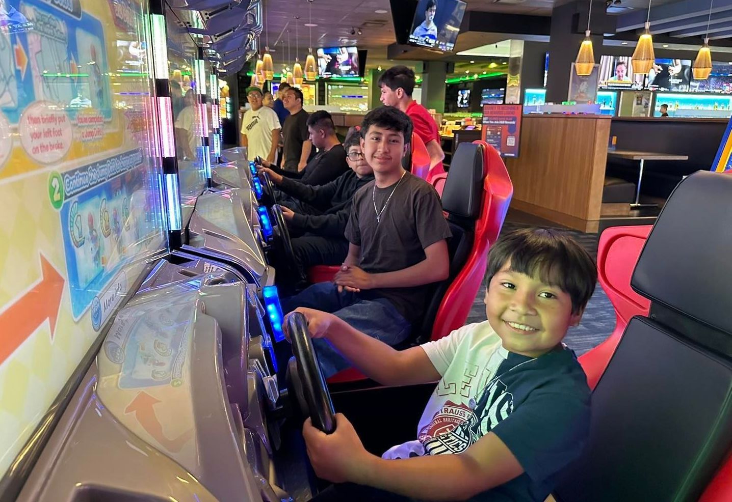 People sitting in arcade racing game seats, smiling at a colorful gaming setup