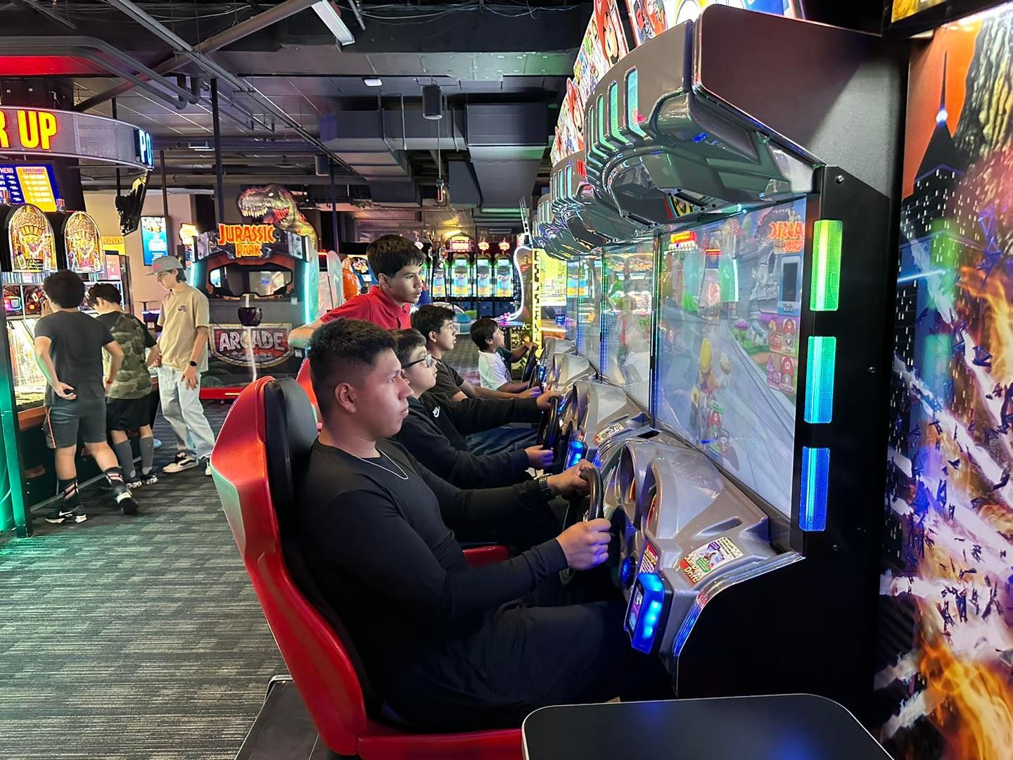 People playing racing arcade games in a brightly lit game room