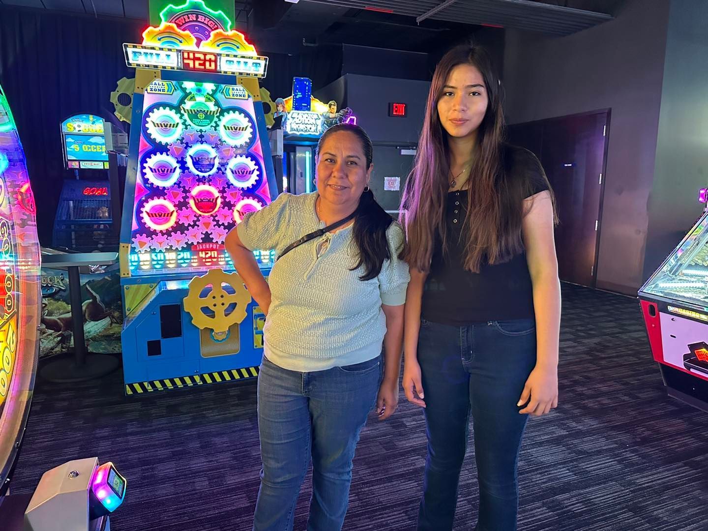 Two people standing in a colorful arcade, with bright game machines in the background.