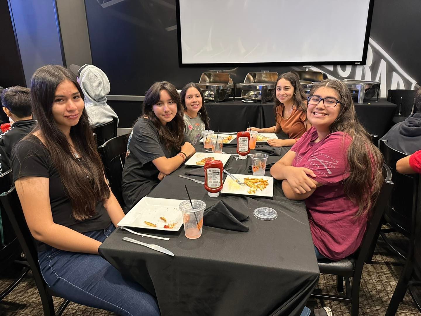 Four friends sitting at a dining table in a conference room, smiling and eating together