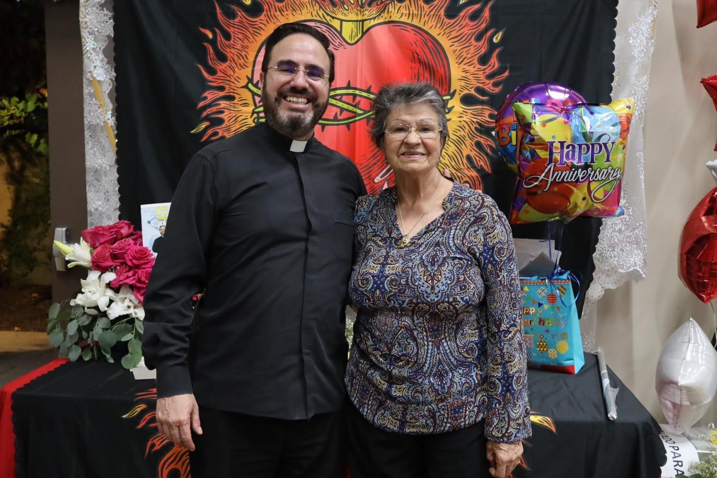 Two people smiling in front of a decorated birthday display with balloons and flowers.