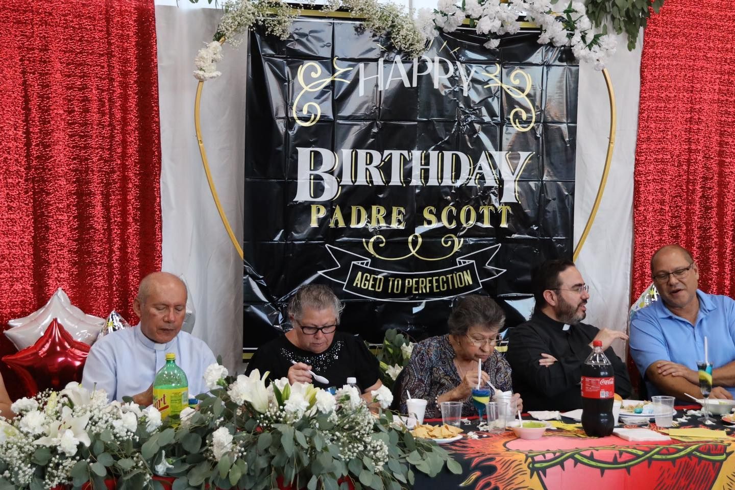 Birthday celebration at a decorated table with five people seated beneath a “Happy Birthday Padre Scout” banner
