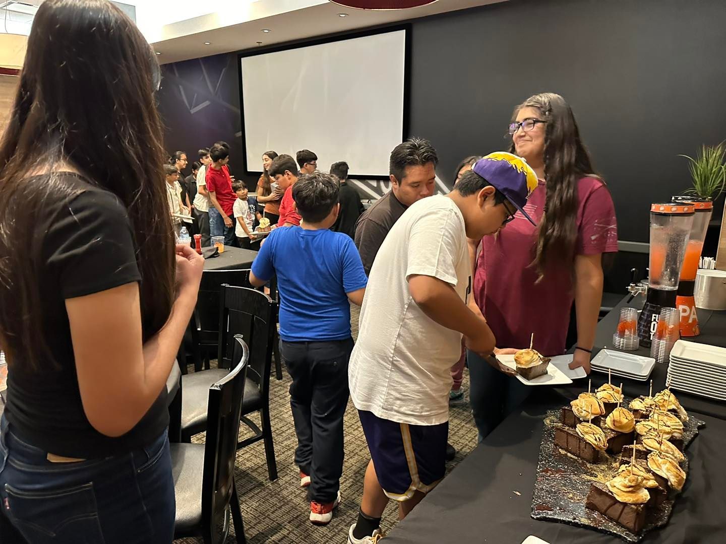 People at a buffet table in a conference room, serving food with trays and cups nearby.
