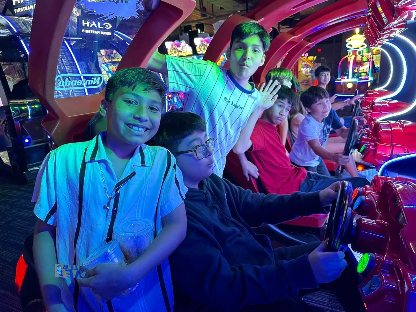 Children riding a colorful indoor amusement ride under neon lights, smiling and waving