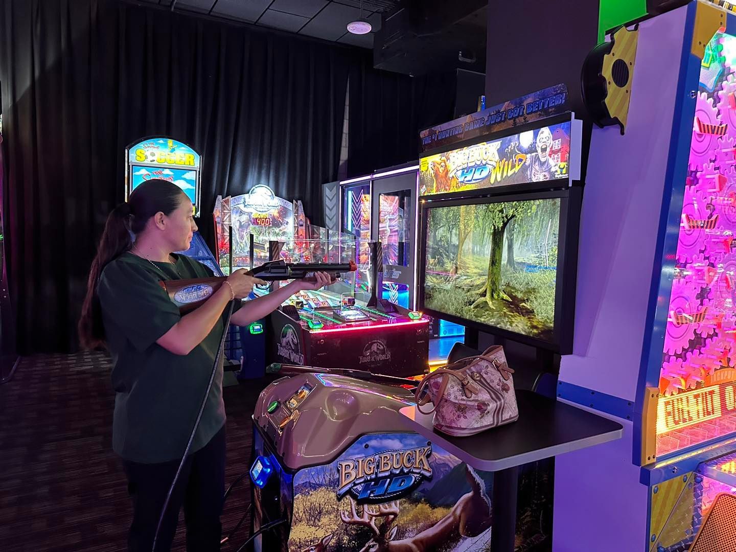 Person playing an arcade game beside a bright claw machine in a dimly lit arcade.