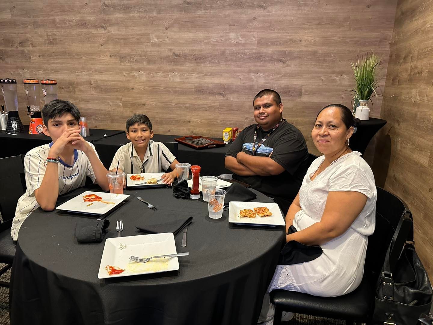 Four people seated around a round table in a restaurant, sharing plates and drinks in a casual meal.