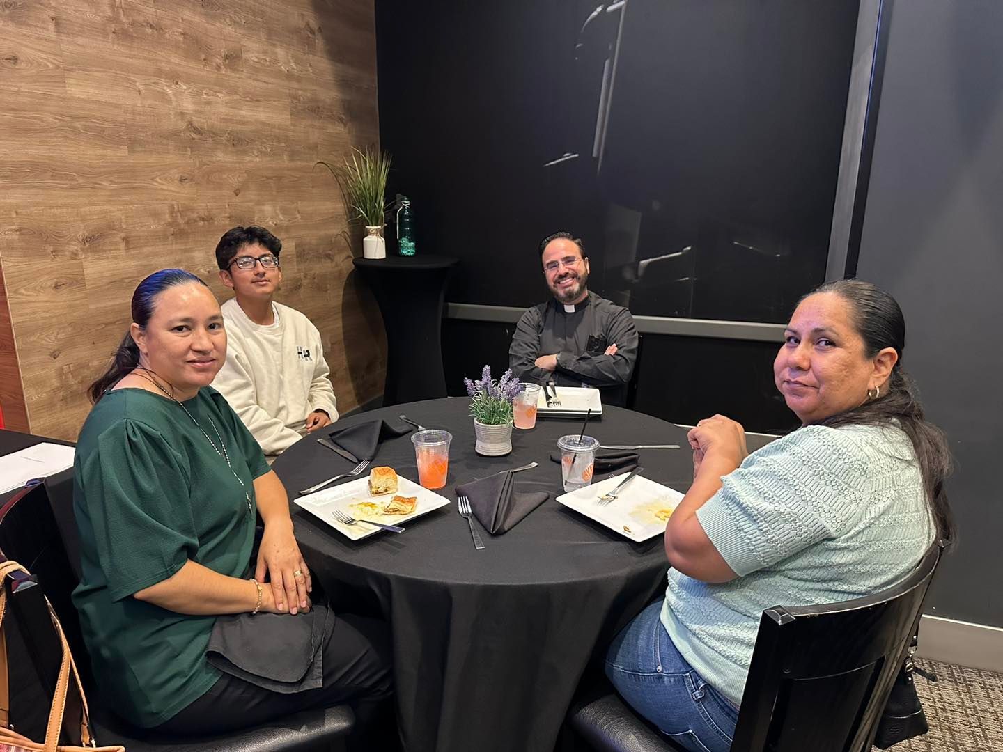 Four people seated around a table in a restaurant, smiling with drinks and plates on the table.