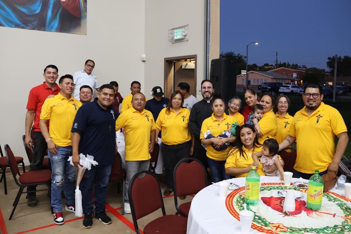 Group of people posing indoors at a festive gathering, many wearing yellow shirts beside a decorated table.