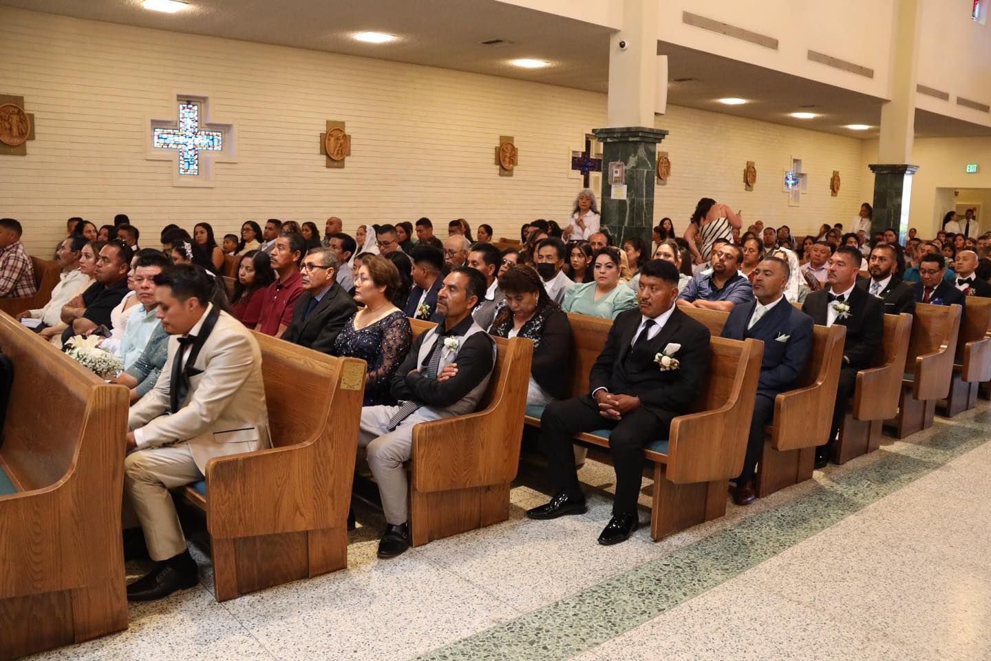 People seated in church pews during a service, with a speaker at the front and stained glass on the wall.