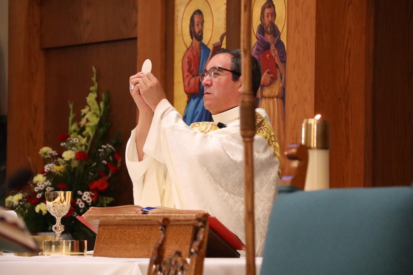 Priest in white vestments raising the chalice during a church service at the altar