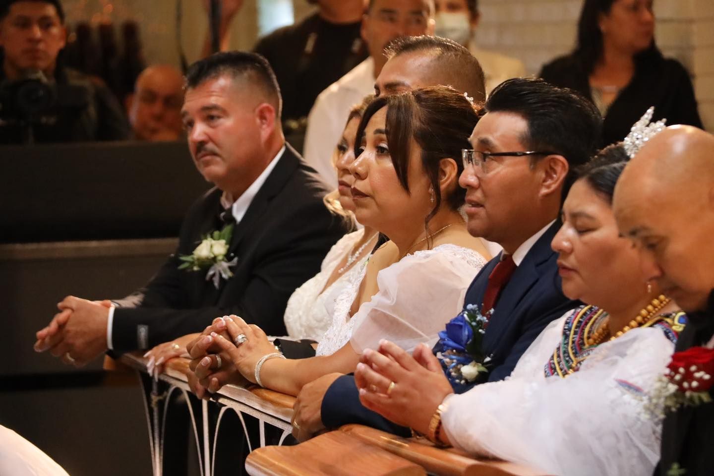 People seated in a church pew, dressed formally and watching an event.