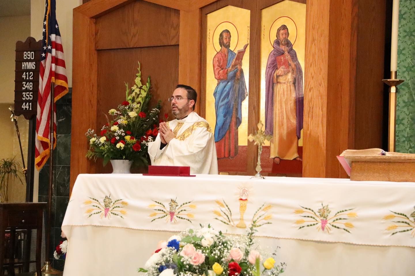 Priest at church altar with floral decorations and religious icons behind him