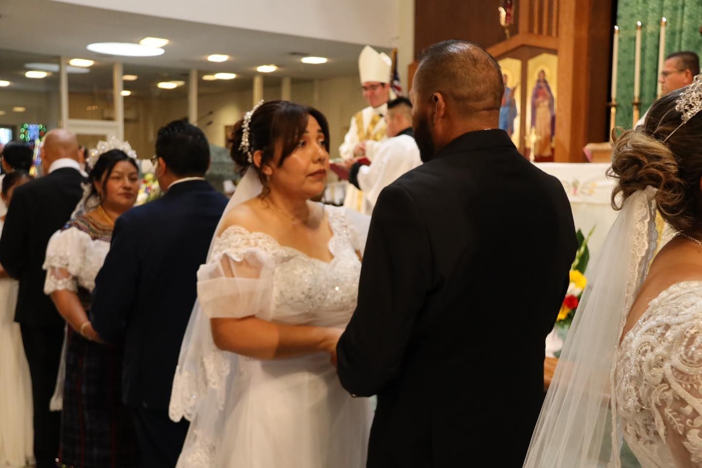 Couple in white wedding attire sharing a moment at an indoor wedding reception