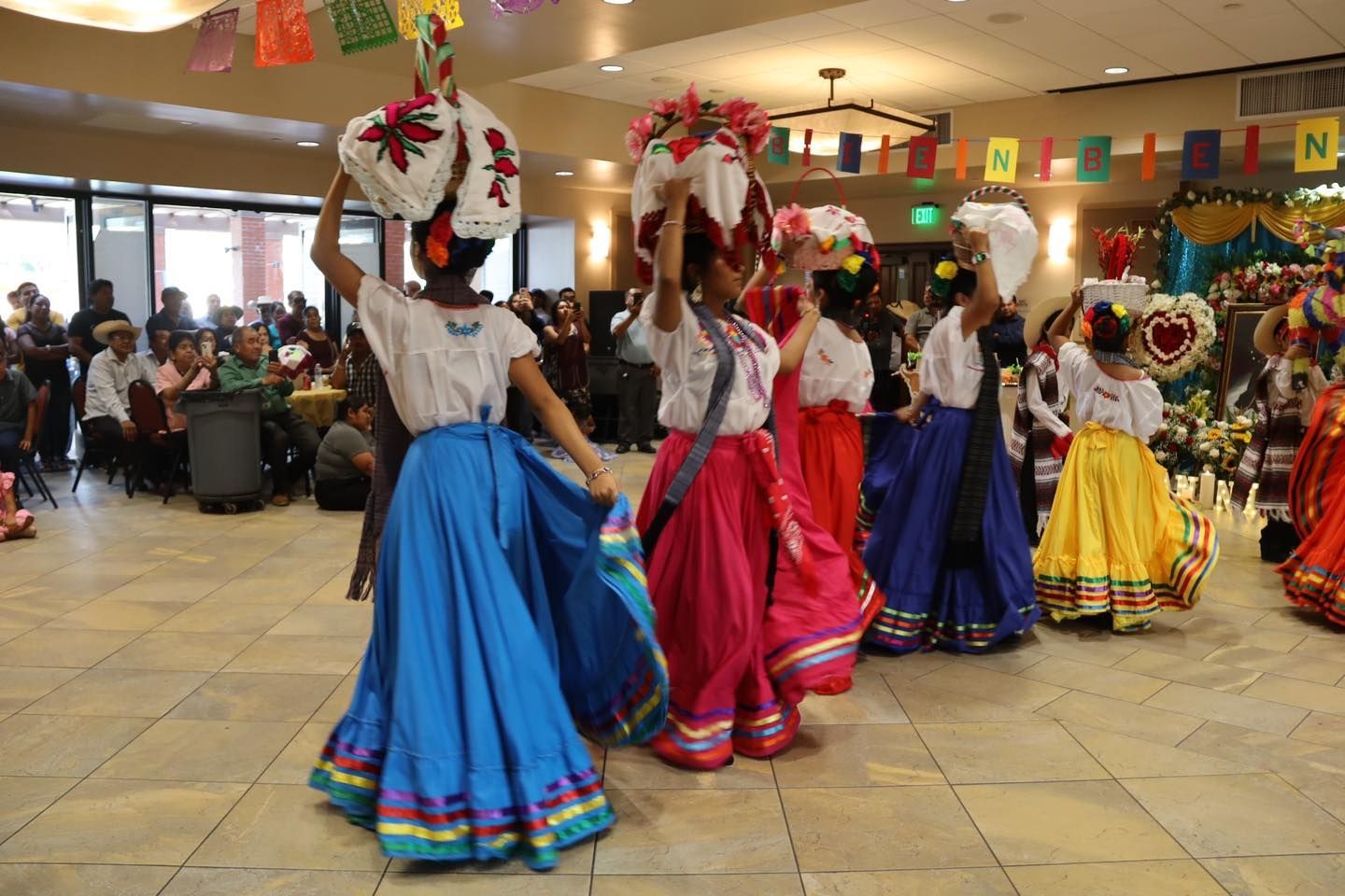 Dancers in colorful skirts perform a traditional dance in a decorated indoor hall