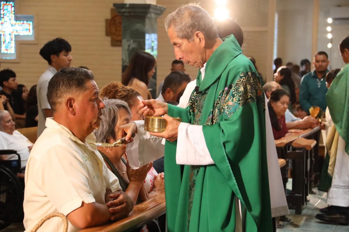 Priest in green vestments giving communion to a man inside a church