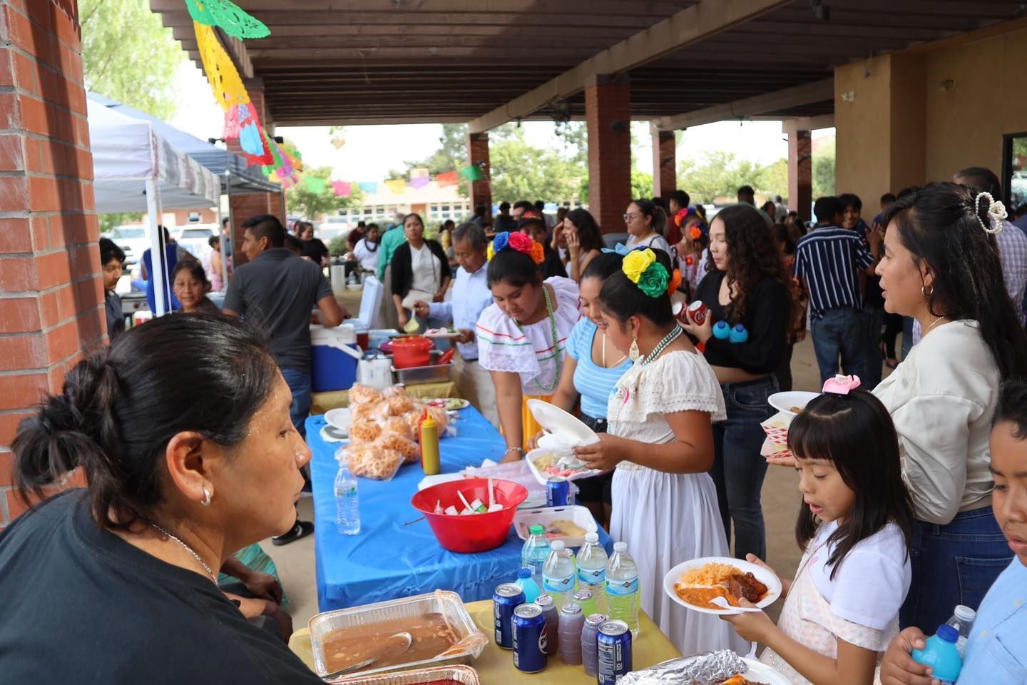 People serving and selecting food at a crowded outdoor buffet under a covered pavilion