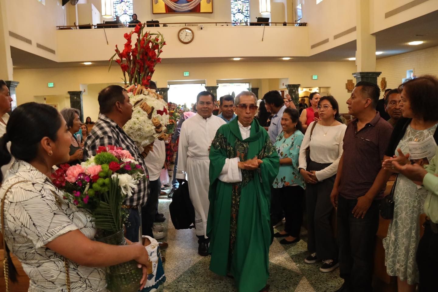 People gathered in a church aisle for a ceremony, with a person in green vestments at center.