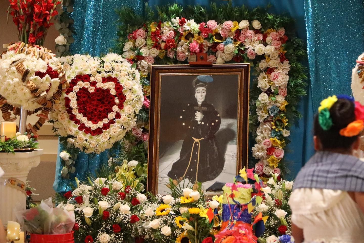 Memorial altar with a framed portrait, heart-shaped flower wreaths, and colorful floral arrangements