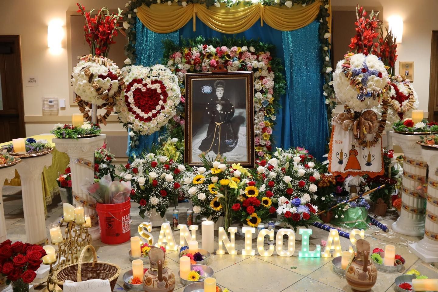 Memorial altar with flowers, candles, and framed portrait, decorated in white, red, and gold