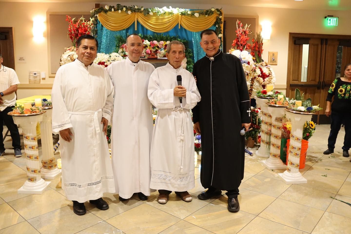 Four people posing in white robes and black attire at a decorated indoor event stage
