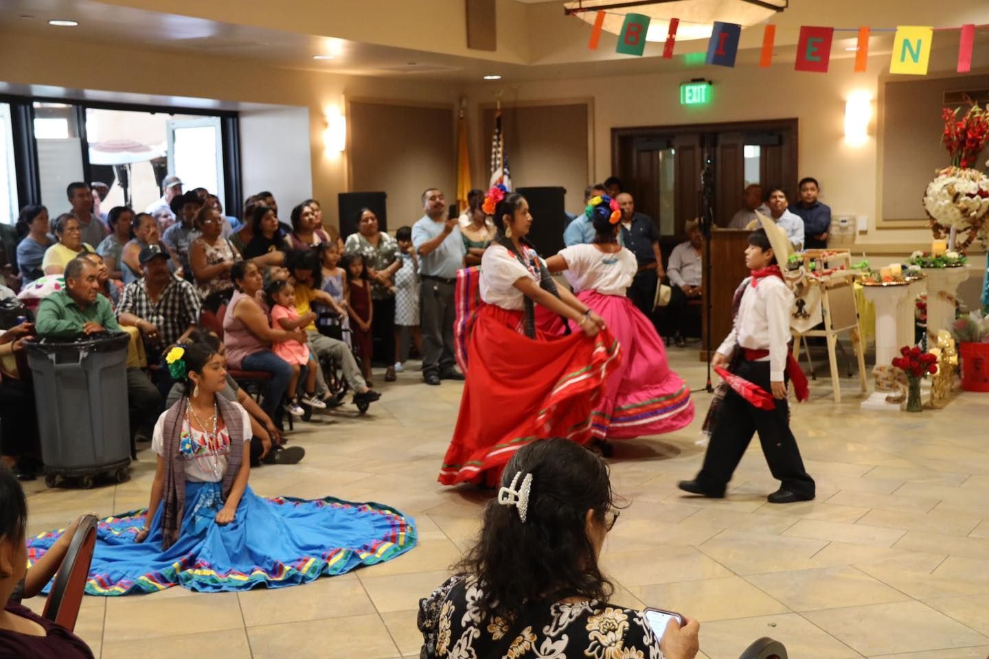 Dance performance in a decorated hall, with performers in red and blue costumes before an audience.