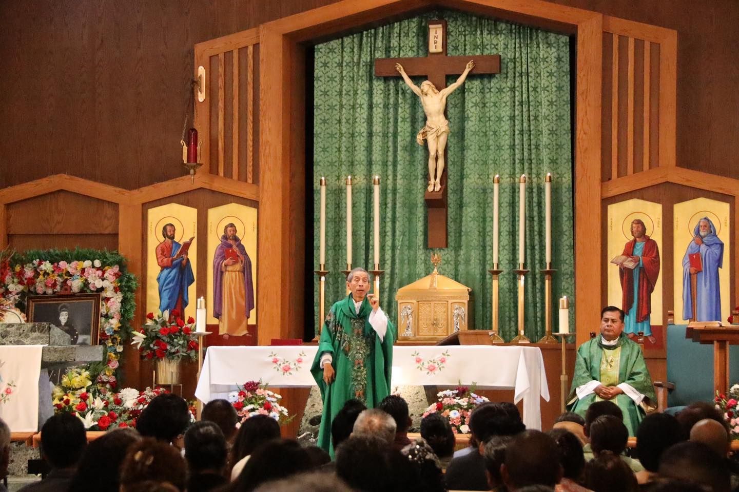 Church altar with crucifix, priests in green vestments, and congregation seated in front.
