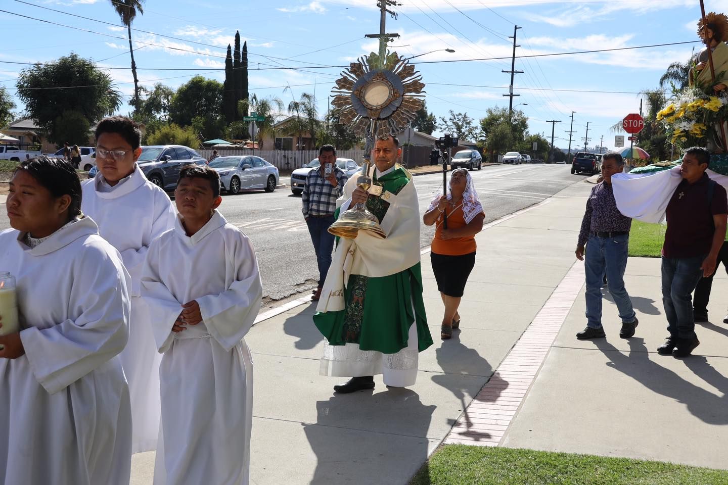 Religious procession with people in white robes carrying a statue along a sunny street