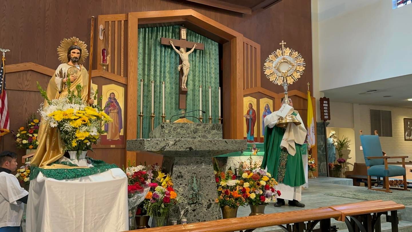 Church altar with crucifix, floral arrangements, and statues in a wood-paneled sanctuary