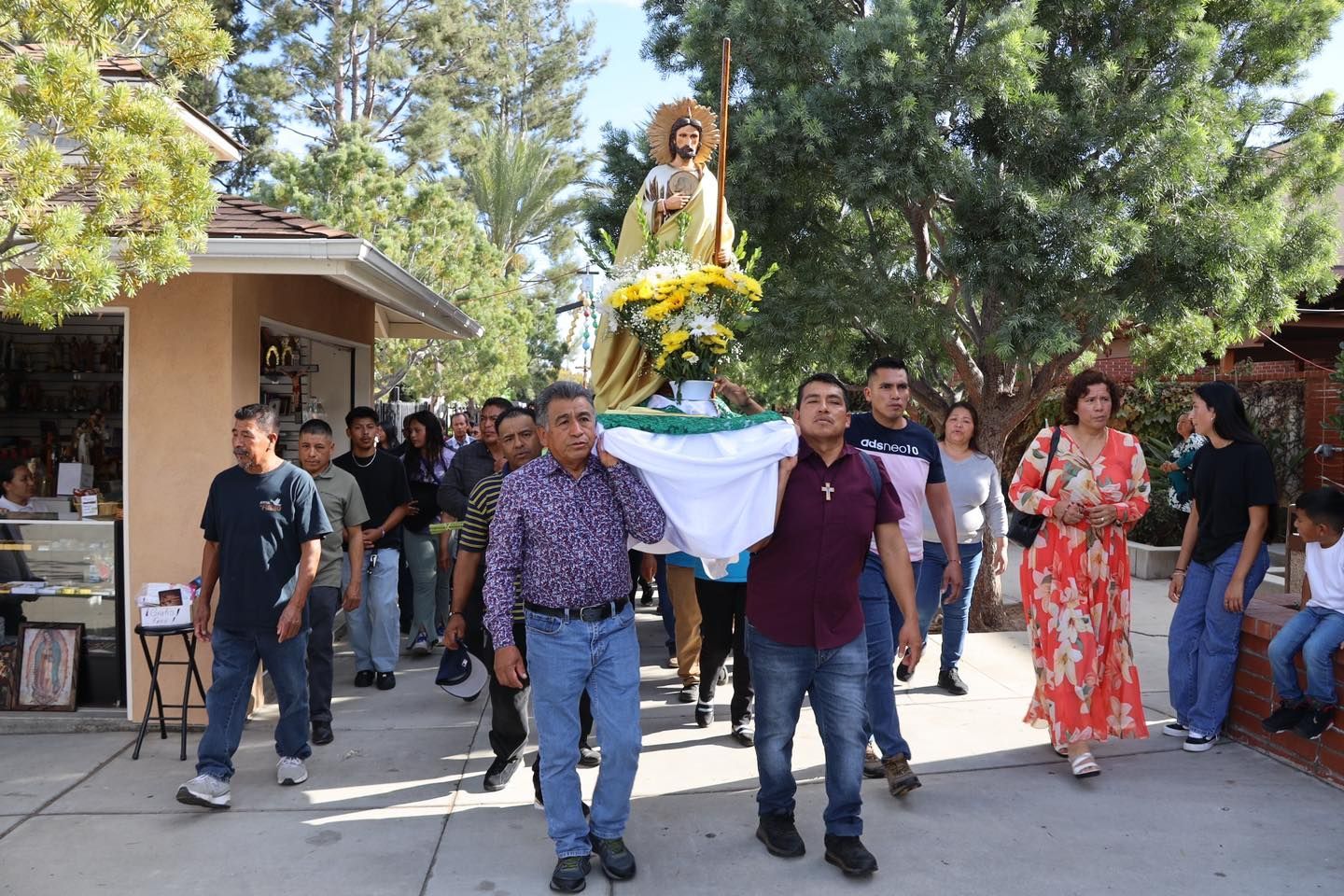 People carrying a decorated statue in an outdoor procession with onlookers nearby
